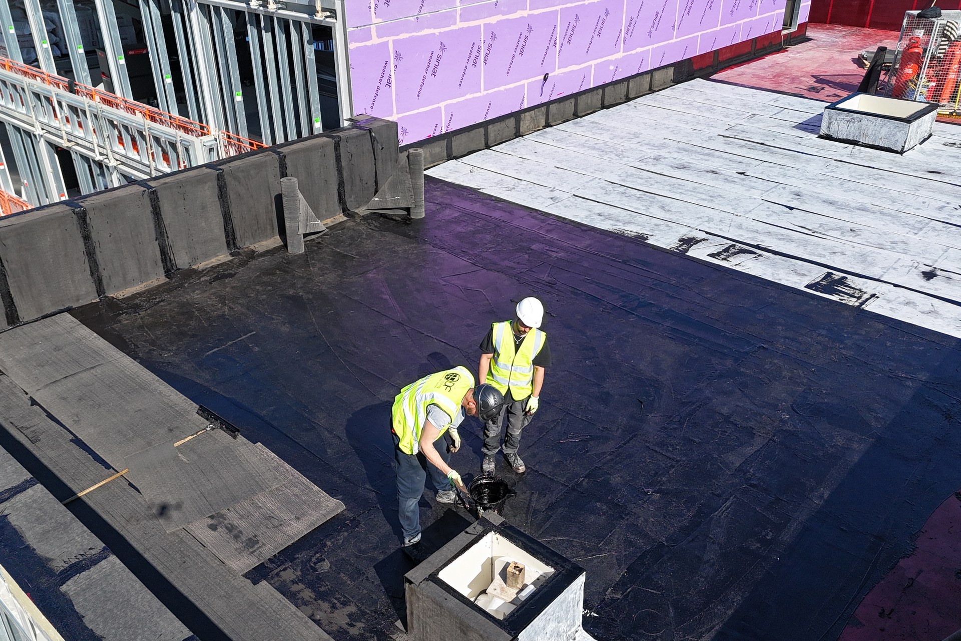 Hot melt waterproofing installation with operatives detailing a commercial roof deck